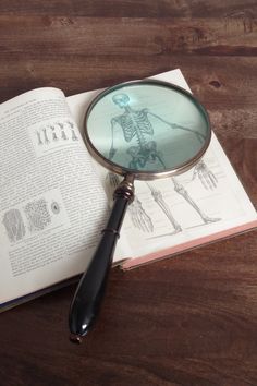 a magnifying glass sitting on top of an open book next to a skeleton