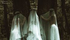 two women dressed in white veils are standing next to each other near a tree