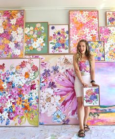 a woman standing next to a wall covered in colorful paintings and flowers on it's walls