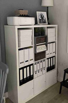 a white bookcase with lots of books and binders on it next to a chair