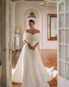 a woman in a white wedding dress is standing by an open door and looking off to the side