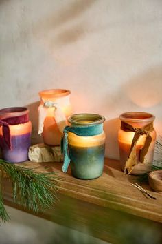 three jars with candles are sitting on a table next to pine branches and other decorations