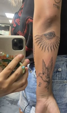 a woman with a bird tattoo on her arm holding a cell phone and taking a selfie