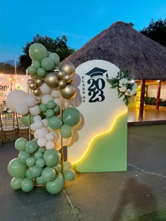 balloons in the shape of a tree are on display at an outdoor event with a sign and tiki hut behind it