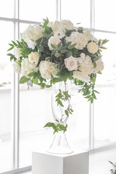 a vase filled with white flowers sitting on top of a table next to a window