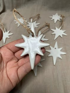 a hand holding a white star ornament in it's left hand, surrounded by other ornaments