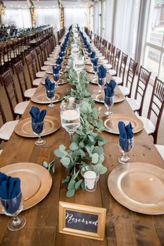 a long wooden table with place settings and plates on it, along with blue napkins