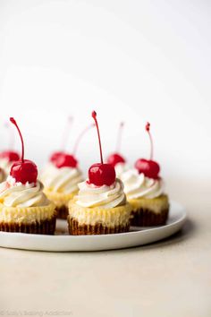 cupcakes with white frosting and cherries on top are sitting on a plate