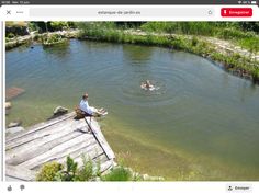 two people are swimming in the water near a wooden dock and green grass on the other side