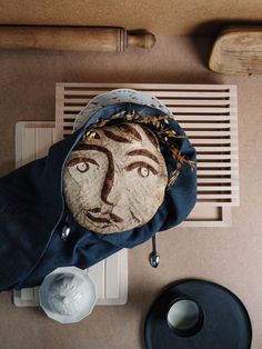 a person's face on a rock next to a bowl and wooden utensils