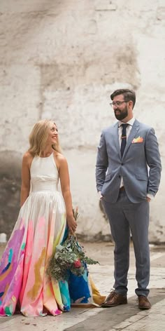 a man and woman standing next to each other in front of a white brick wall