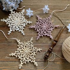 crocheted snowflakes are displayed on a wooden surface with yarn and thread