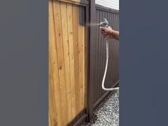 a person is spraying water onto the side of a fence with a hose attached to it