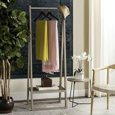 a rack with clothes hanging on it next to a potted plant and a chair