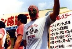 a man wearing a wrestling mask and holding his fist up in front of a group of people