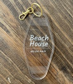 a clear acrylic keychain with the words beach house on it sitting on a wooden surface