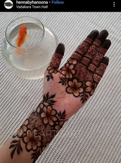 henna tattoo on hand next to a glass of water and goldfish in bowl