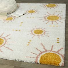 a white rug with yellow and pink flowers on it, next to a book sitting on the floor