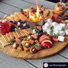 a wooden platter filled with cheese, crackers, fruit and marshmallows