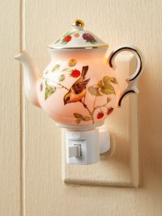 a teapot shaped light switch cover with flowers and birds painted on it, sitting on a wall