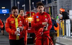 two men in red and yellow racing suits are walking down the street while one man is holding a camera