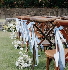 rows of wooden chairs with blue sashes and flowers in the grass at an outdoor ceremony