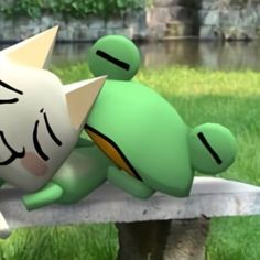 a green stuffed animal laying on top of a cement bench in the grass next to a body of water