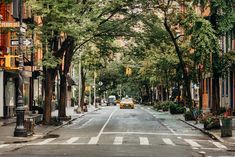 an empty city street with trees lining both sides and cars driving down the road on either side