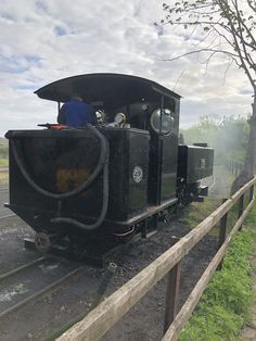 an old fashioned train traveling down tracks next to a wooden rail road fence and tree