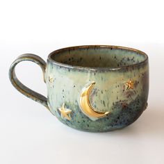 a ceramic cup with gold stars and moon designs on it's rim, sitting on a white surface