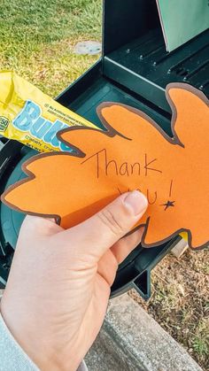 a person holding up an orange piece of paper with the words thank you written on it