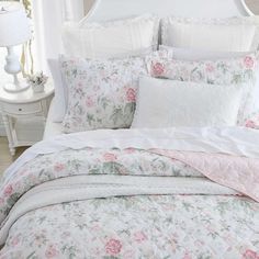 a white bed with pink and green flowers on the comforter, pillows and pillow cases