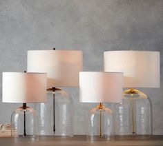 three clear glass lamps sitting on top of a wooden table next to a white lamp shade