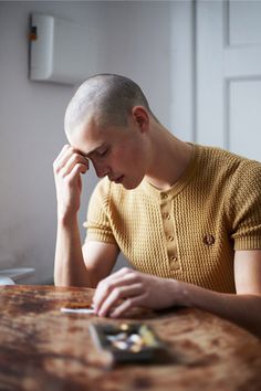 a man sitting at a table with his hand on his head and looking at something in front of him