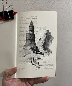 a hand holding an open book with a drawing of a lighthouse and people on it