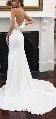 a woman in a white dress is standing near a fireplace and looking at the back of her dress