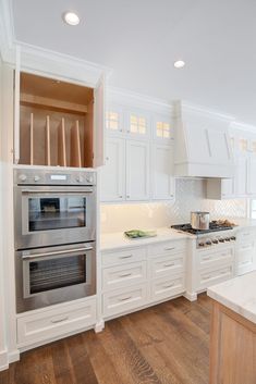 a kitchen with white cabinets and stainless steel ovens in the center, along with wooden flooring