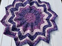 a purple and white crocheted blanket sitting on top of a wooden floor