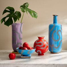 three colorful vases sitting next to each other on a white counter top with fruit and vegetables in them