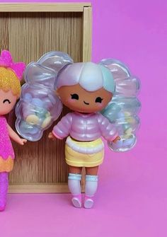 two little dolls standing next to each other in front of a wooden frame on a pink background