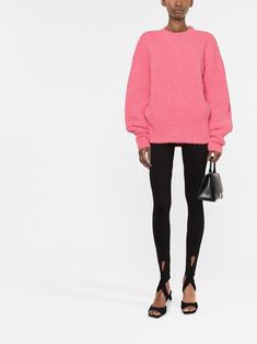 a woman in a pink sweater and black leggings stands against a white background