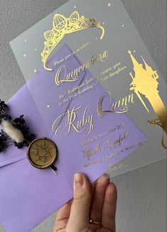 a person holding up two purple and gold wedding cards with a wax stamp on it