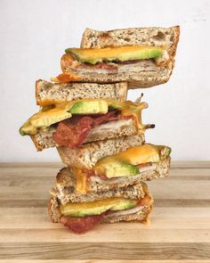 a stack of sandwiches with bacon, avocado and cheese on them sitting on top of a wooden table