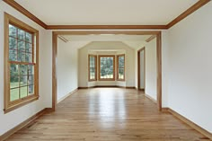 an empty room with wood floors and large windows in the center is seen from the hallway