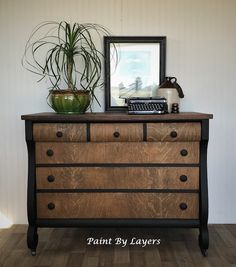 an old dresser with some plants on top and a framed photo in the corner next to it