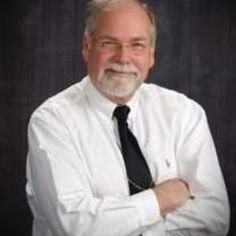 an older man wearing a white shirt and black tie with his arms crossed in front of him