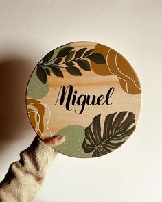 a person holding up a wooden sign with leaves on it that says nignel