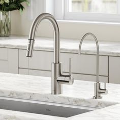 a stainless steel kitchen sink and faucet with white marble countertops in front of a window