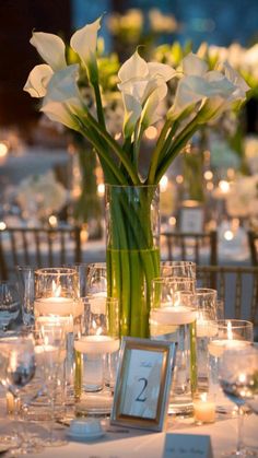 a vase filled with white flowers sitting on top of a table covered in glasses and candles