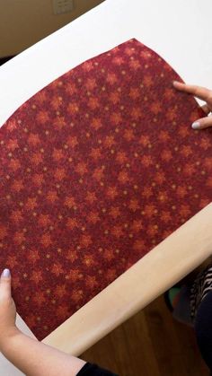 a woman is holding up a piece of fabric on top of a wooden frame with red and gold designs